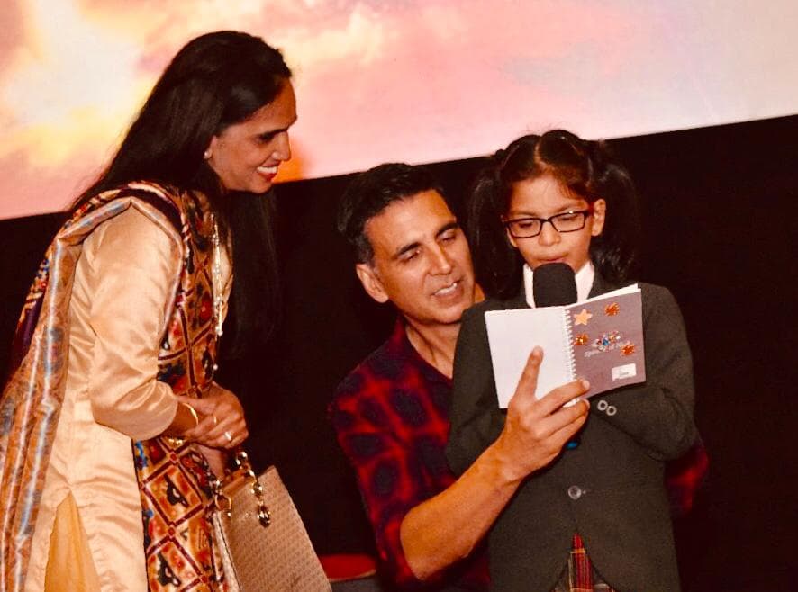 Akshay kumar, holding a student and reading a book, at the Education World India School Merit Awards 2019